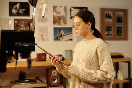 Side view portrait of teenage girl looking at film negatives while working on analog photography in...