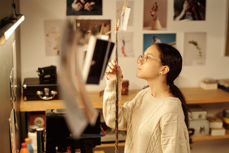 Side view portrait of teenage girl looking at developed film strip in bright photography studio young photographer working with analog photography copy spaceの写真素材