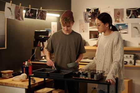 Portrait of teenage boy and girl working together developing photo prints in studio and mixing...