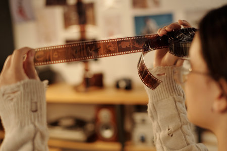 Close up of young teenage girl carefully holding film negatives to light while analyzing developed images in darkroom copy spaceの写真素材