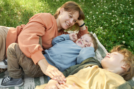 Candid scene of happy family mother and two boys lying on picnic blanket together and having fun...