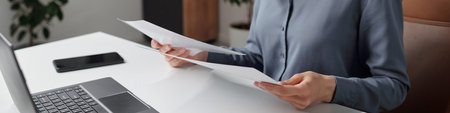 Header image of young businesswoman reading documents wearing glasses while sitting at workplace in office copy spaceの写真素材