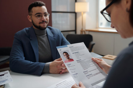Over shoulder shot of recruiter holding CV during job interview with smiling candidate in defocused...