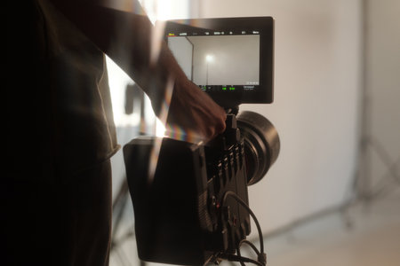 Closeup of production crew holding camera and viewing scene composition on monitor during video shoot in studioの写真素材