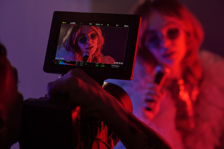 Closeup of filming monitor showing singer with microphone and sunglasses performing under red and purple neon lightsの写真素材