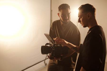 Side angle of young videographer and assistant director analyzing footage on set during video productionの写真素材