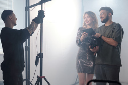 Waist up portrait of smiling actress and director reviewing footage on camera monitor while lighting...