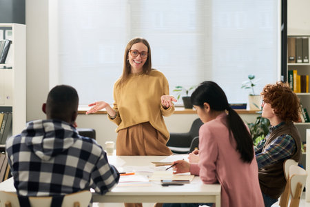 Young smiling educator explaining concepts to diverse group of students studying foreign languages in classroom settingの写真素材