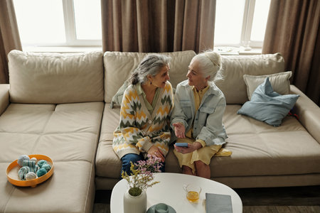 Elderly women sitting on a beige couch and having a conversation They are sitting around a table with coffee cups and decorative itemsの写真素材