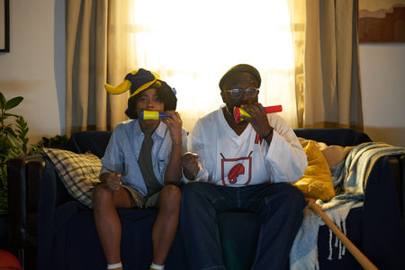 Portrait of father and son enjoying time together, playing musical instruments on sofa, with warm...