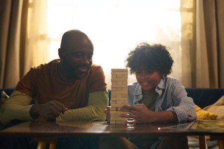 Black person interacting with child while playing Tower game, demonstrating concentration and...