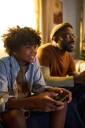 Smiling father and son sitting on couch, playing video games together, enjoying quality bonding time...