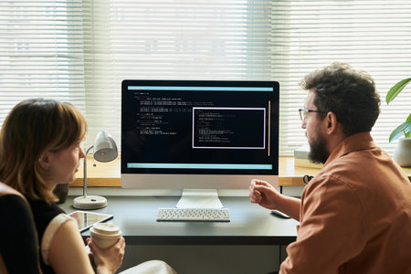 Caucasian young adult woman and Caucasian middle aged man collaborating at desk, analyzing neural network code displayed on computer monitor, discussing software development processの写真素材