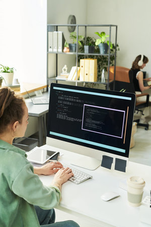 Young adult Caucasian woman developing neural network code on desktop computer in modern office,...