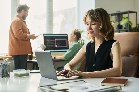 Caucasian young adult woman working on laptop developing neural network while multiethnic young adult man and woman collaborating in backgroundの写真素材