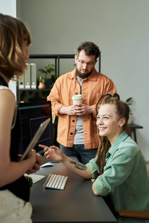 Woman with dreadlocks sitting at desk smiling and discussing neural network development with man and...