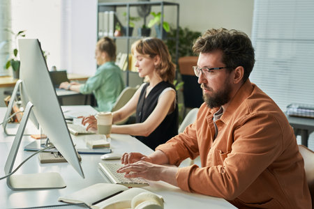 Caucasian young adult man developing neural network on desktop computer with diverse colleagues in backgroundの写真素材