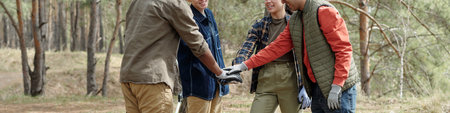 Group of multiethnic teenagers standing outdoors joining hands in teamwork gesture, smiling and...