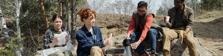 Group of multiethnic young adults sitting outdoors sharing food and drinks during picnic, smiling...