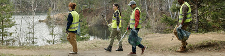Group of young adult and middle aged multiethnic volunteers walking along forest path near lake...