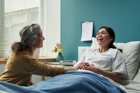 Middle aged Caucasian woman sitting beside hospital bed holding hand of young pregnant woman lying...
