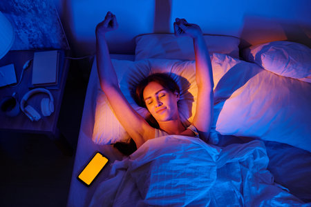 Woman lying in bed stretching arms after waking up, eyes closed, illuminated by warm light,...