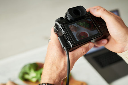 Male hands holding digital camera capturing food photography scene, focusing on healthy meal with...