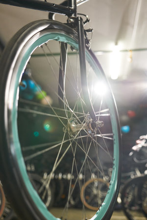 Close up showing front wheel of bicycle with turquoise rim in indoor bike shop, metal spokes and hub clearly visible, multiple bicycles blurred in background, focus on wheel structureの写真素材