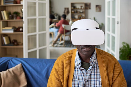 Mature man wearing virtual reality headset sitting indoors, interacting with digital content