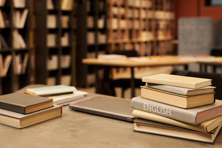 Stack of books including English language textbook on table in library with shelves full of books in backgroundの写真素材