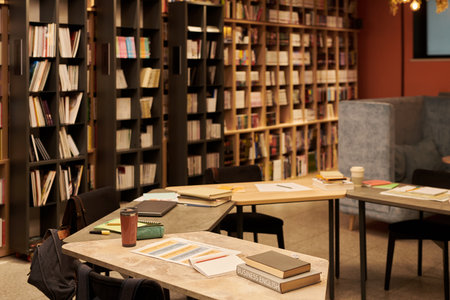 Empty library interior showing bookshelves filled with books, several tables with open notebooks arranged for study sessionの写真素材
