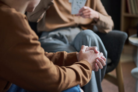 Young man sitting with hands clasped, listening attentively to adult woman holding cards during...
