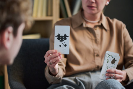 Adult woman holding inkblot card conducting group therapy session with teenage boy in foreground focusing on psychological assessment activityの写真素材