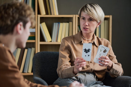 Adult woman therapist holding inkblot cards with teenager during group therapy session, both seated...
