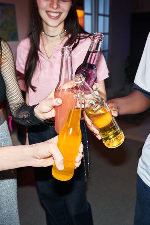 Group of young people and teenagers clinking glass bottles with colorful drinks during celebration,...
