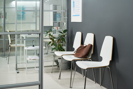 Empty waiting area featuring row of chairs against dark wall, brown leather handbag resting on one...