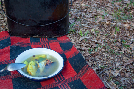 Fish soup in iron plat stands on plaid blanket with pot on background

の写真素材