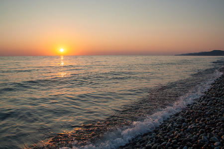 Sunset on sea pebble beach. Evening on sea beach with wavesの写真素材