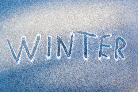 The inscription "Winter" drawn by a finger on a blue background. The concept of the beginning of winterの写真素材