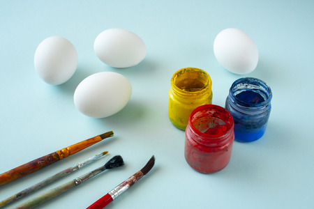 A set of white clean eggs, blue, yellow and red paints and brushes on bright background. Easter symbols. Easter eggs, painting eggs, easter illustration image.  Easter entertainment concept, easter traditionの写真素材
