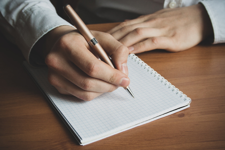 a man with a pen in his hand writes in a notebook close upの写真素材