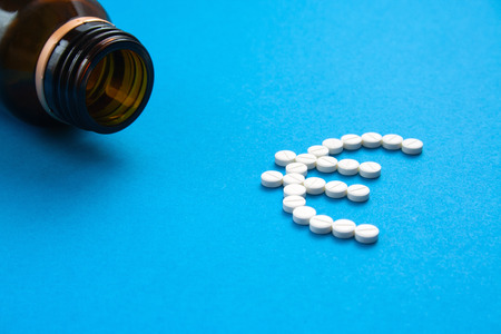 white pills in the shape of a euro are scattered on a blue background next to a dark bottle.の写真素材