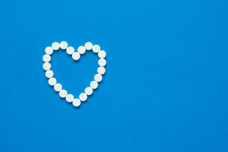 white pills in the shape of a heart are scattered on a blue background. Top viewの写真素材