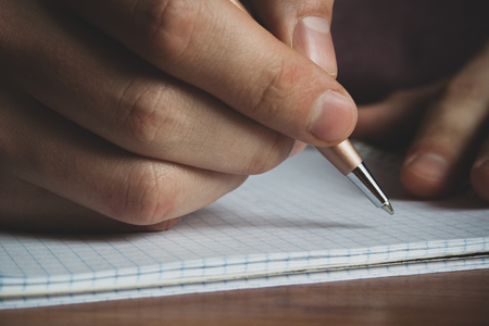 a man with a pen in his hand writes in a notebook close upの写真素材