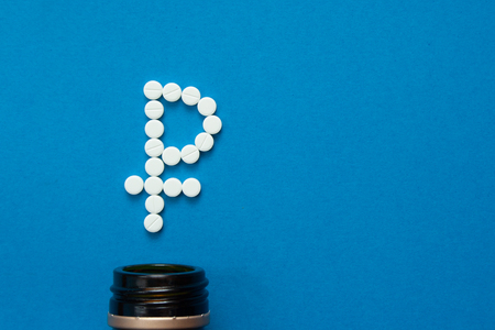 white pills in the shape of a ruble are scattered on a blue background next to a dark bottle.の写真素材