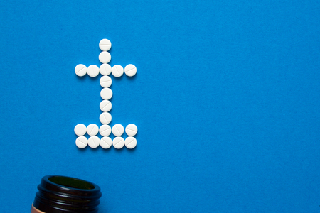 white pills in the shape of a grave cross are scattered on a blue background next to a dark bottle. Depression, harm of drugs concepts. Top view with copyspaceの写真素材