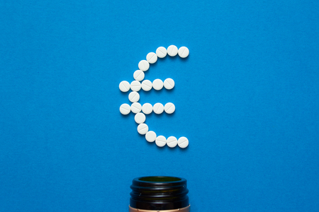 white pills in the shape of a euro are scattered on a blue background next to a dark bottle.の写真素材