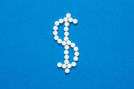 white pills in the shape of a dollar are scattered on a blue background. Top viewの写真素材