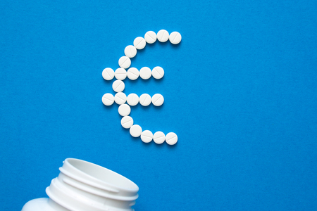 white pills in the shape of a euro are scattered on a blue background next to a dark bottle.の写真素材