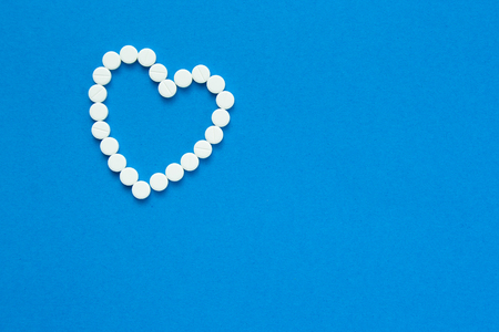 white pills in the shape of a heart are scattered on a blue background. Top viewの写真素材